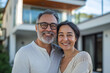 © GustavsMD - Mature couple in casual clothes smiles warmly outside their modern home, embodying happiness and togetherness in a serene environment.
