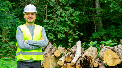 Portrait man forestry worker in protective workwear in front of wood lumber cut tree. Male forestry engineer, inspector appraiser of felled timber, working in the forest at logging.