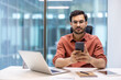 © Liubomir - Serious businessman using smartphone in modern office. He is seated at desk with laptop, notebook and pen. Scene reflects technology, professionalism, focus.