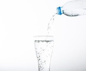 Wall Mural - Pouring drinking water into a glass, isolated on white background. Plastic water bottle and pouring water into a glass, isolated on white background.