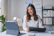 © amnaj - Asian businesswoman is smiling while working from her home office and using a tablet computer for a video conference call