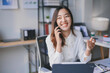 © amnaj - Asian businesswoman is working at her desk and discussing on the phone with a big smile