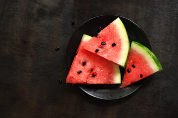 Slices of juicy ripe watermelon, watermelon on a black plate on a dark wooden background. Top view. A refreshing summer fruit. Delicious watermelon