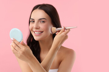 Wall Mural - Beautiful makeup. Smiling woman applying blush with brush on pink background, space for text