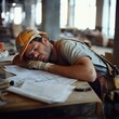 © Oatthapon - A construction worker slumped over a table, with blueprints scattered around, taking a brief nap