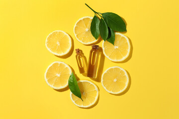 Wall Mural - Bottles of essential oils, lemon and green leaves on yellow background, flat lay