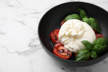 Delicious burrata cheese, tomatoes and basil in bowl on white marble table, closeup. Space for text