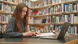 © Pavel - Serious attractive Caucasian young adult female student uses laptop for online learning, socializing in the library, teacher professional development, higher education, working on a science project