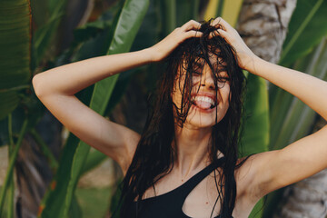 Poster - Tropical beauty concept young woman with wet hair standing in front of palm tree with hands on head