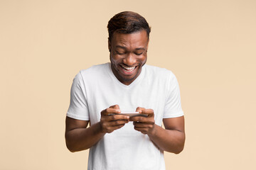 Aufkleber - Mobile Gaming. Excited Black Man Using Cellphone Playing Online Games Standing Over Yellow Background. Studio Shot