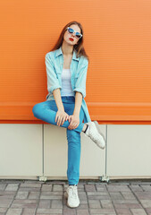 Wall Mural - Portrait of modern stylish young woman in white glasses, casual clothing posing on orange background