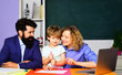 © Svitlana - Little boy from elementary school doing schoolwork with teachers man and woman. Private lesson. Parents and son schooling together. Cute child from primary school make homework with father and mother.