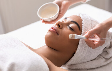 Wall Mural - Spa therapist applying face mask on african woman skin, closeup