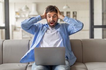 Poster - Shocked bearded man wearing casual outfit sitting on couch at home, looking at laptop screen on his lap and touching his head, got breathtaking news