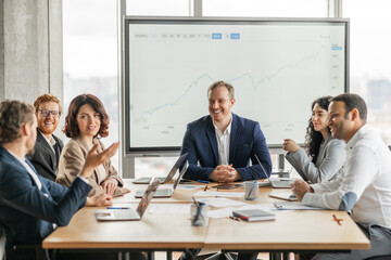 Aufkleber - A group of business professionals sit around a large wooden conference table, engaged in a meeting. They are looking at a large screen behind them displaying a projected growth graph