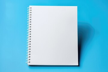 Poster - A simple and clean scene of a white spiral notebook placed on a blue surface, ready for writing or drawing