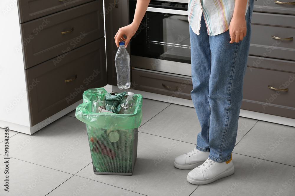 Woman putting plastic bottle into trash bin in kitchen