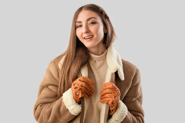 Wall Mural - Beautiful young woman in leather gloves and sheepskin on light background