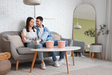 Wall Mural - Happy young couple with popcorn at home