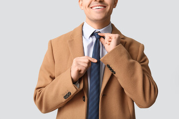 Sticker - Smiling young man straightening his tie on white background. Closeup