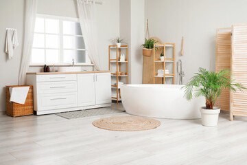 Canvas Print - Interior of light bathroom with bathtub, houseplant and white furniture