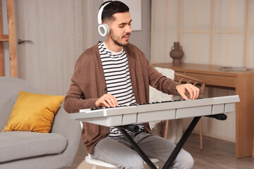 Wall Mural - Young bearded man in headphones playing synthesizer at home