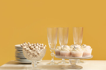 Wall Mural - Table with different sweets, plates and glasses for birthday party against yellow wall