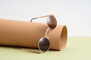 Wall Mural - Stylish sunglasses and rolled paper on green background, closeup