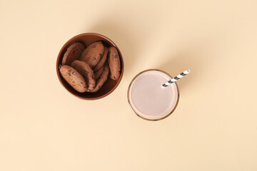 Wall Mural - Glass of sweet chocolate milk and bowl with tasty cookies on beige background