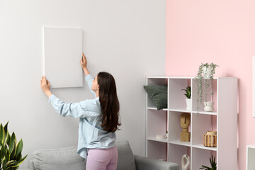 Wall Mural - Young woman hanging empty canvas on white wall in living room