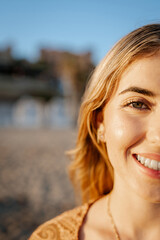 Wall Mural - Portrait of one happy young beautiful woman smiling looking at the camera with big blue and green eyes. Female girl at the beach close up face.