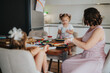 © qunica.com - Mother and two children at a kitchen table, enjoying a family meal and engaging in crafts. Cozy home setting, depicting family bonding and togetherness.