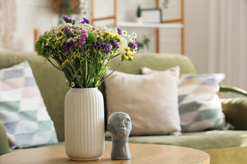 Canvas Print - Wild flowers in vase and stone human head on coffee table in living room. Closeup