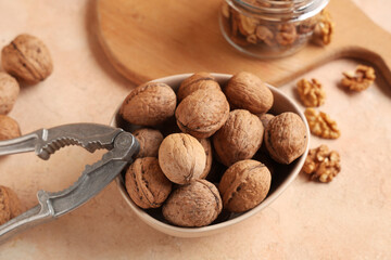 Canvas Print - Bowl with tasty walnuts and nutcracker on beige background