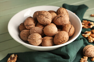 Canvas Print - Bowl with tasty walnuts on green wooden background