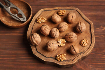 Canvas Print - Board with tasty walnuts and nutcracker on wooden background