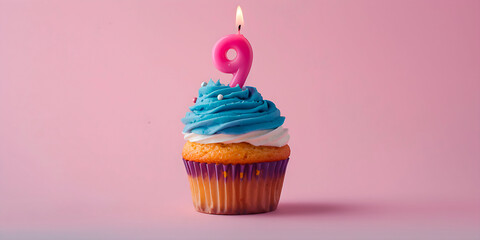 A cupcake with a lit candle on top of it with the number nine on it. The cupcake is blue and white and is sitting on a pink background