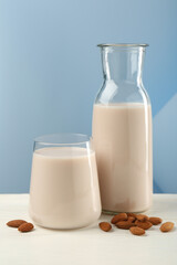 Wall Mural - Fresh almond milk in carafe, glass and nuts on white wooden table