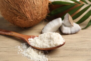 Fresh coconut flour in spoon, nuts and palm leaf on wooden table, closeup