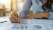 © Marnee - A person analyzing data with graphs and charts, holding a pen, surrounded by financial documents in a modern office setting.