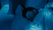 © golubovy - Exhausted man experiencing loneliness insomnia lying awake in bed under dim blue lighting.