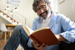 © Daniel - Happy mature man with glasses relaxing at home reading a book.