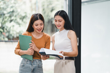 Wall Mural - Two businesswomen engaged in discussion while reviewing documents on clipboard in modern office.