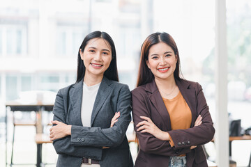 Two confident Asian businesswomen stand with crossed arms in office.