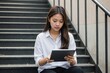 © ThomasLENNE - Front view of a young Asian female student using a tablet computer on a staircase