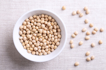 Wall Mural - Dried soybeans, also soy beans or soya beans in a white bowl on linen fabric. Whole and raw seeds of the legume and oilseed Glycine max, with a very high protein and oil content. Close-up from above.