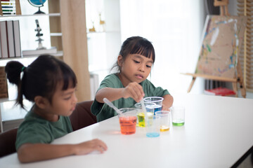 two young girls are sitting at a table, playing with a science experiment