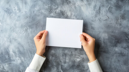 Wall Mural - A minimalistic photograph of hands holding a blank white sheet of paper, shot from a top-down perspective, set against a smooth gray concrete background