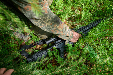 Hunter with rifle wearing camouflage suit sitting in ambush. Camouflaged sniper in the forest in ambush. Military man hide in the woods with rifle.