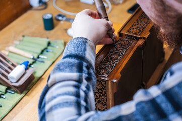 Wall Mural - male artisan carpenter carves a pattern on wooden casket in a workshop in Uzbekistan